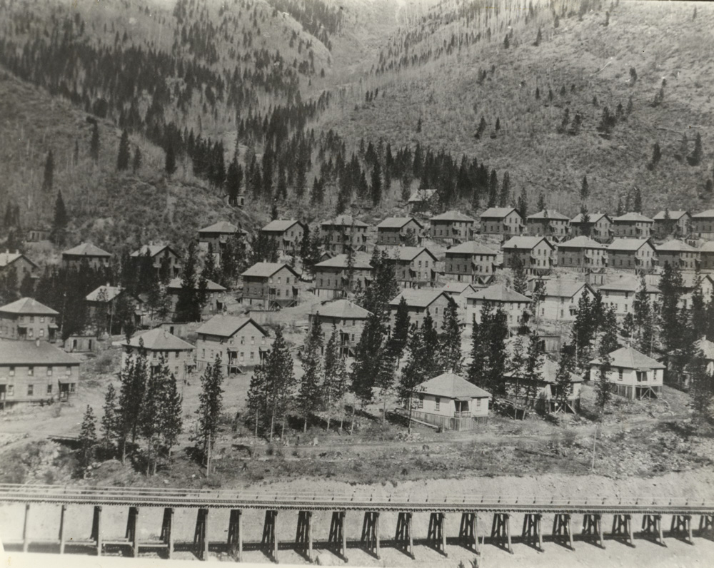 A row of coke ovens in front of rows of one-story cottages and two- story boarding houses.