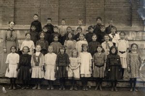 A group of students standing in four rows in front of a brick school.