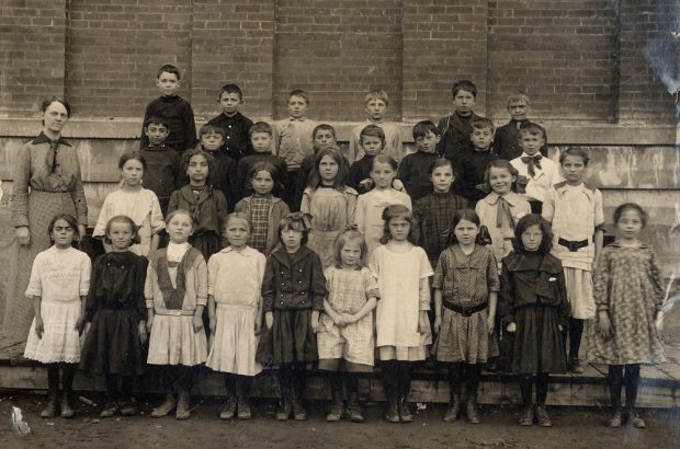 A group of students standing in four rows in front of a brick school.