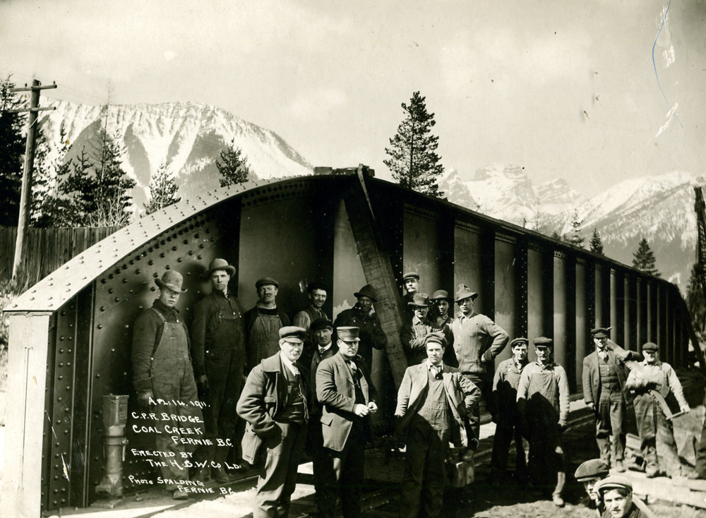 Two rows of men standing in front of a railroad bridge.