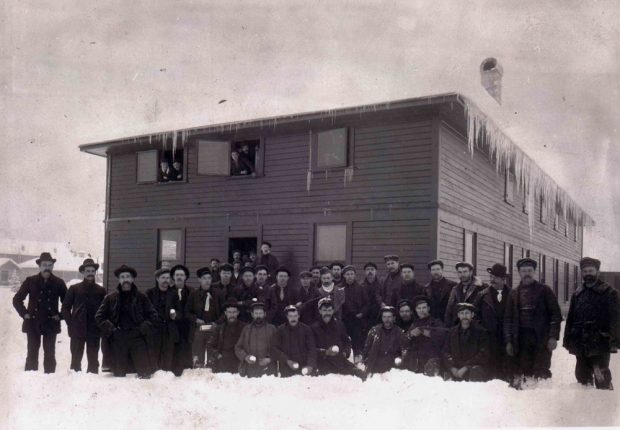 A large group of men standing in front of a two story house in the winter.