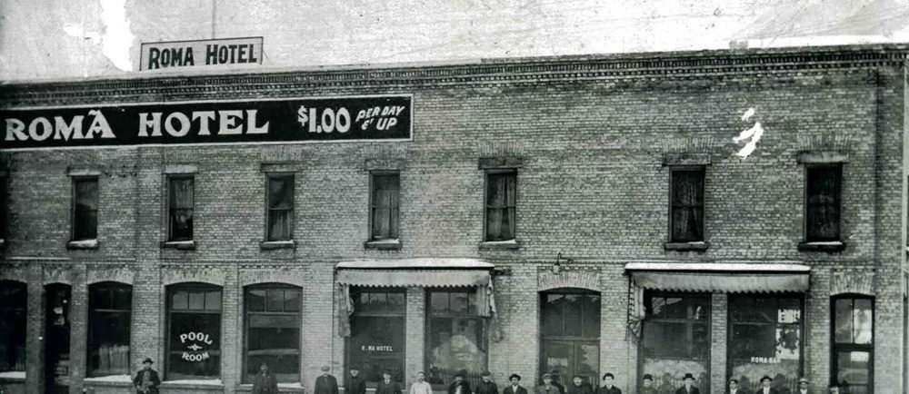 A group of men standing in front of the Roma Hotel in winter.