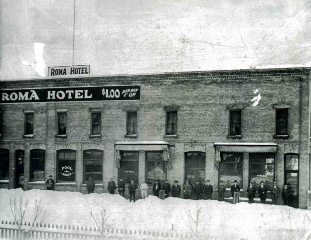 A group of men standing in front of the Roma Hotel in winter.
