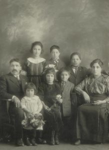 Une famille avec papa assis à gauche, maman assise à droite et six enfants debout entre eux.