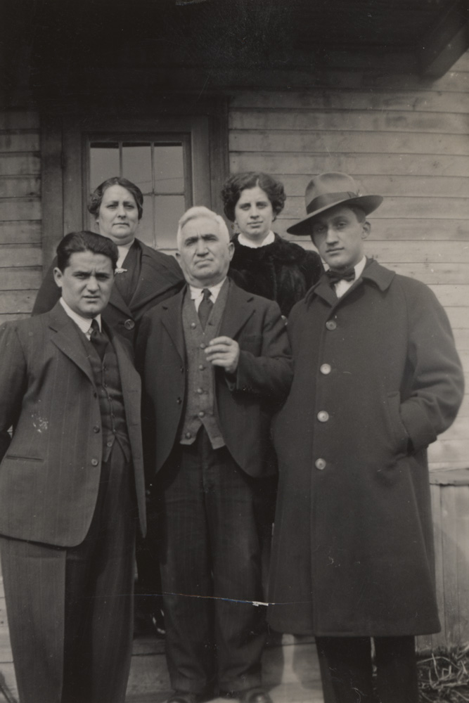 Group of three men and two women standing in front of a house.