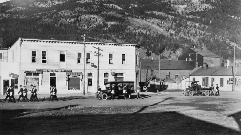 Alberta Hotel building with a car and a group of men marching in two in front.
