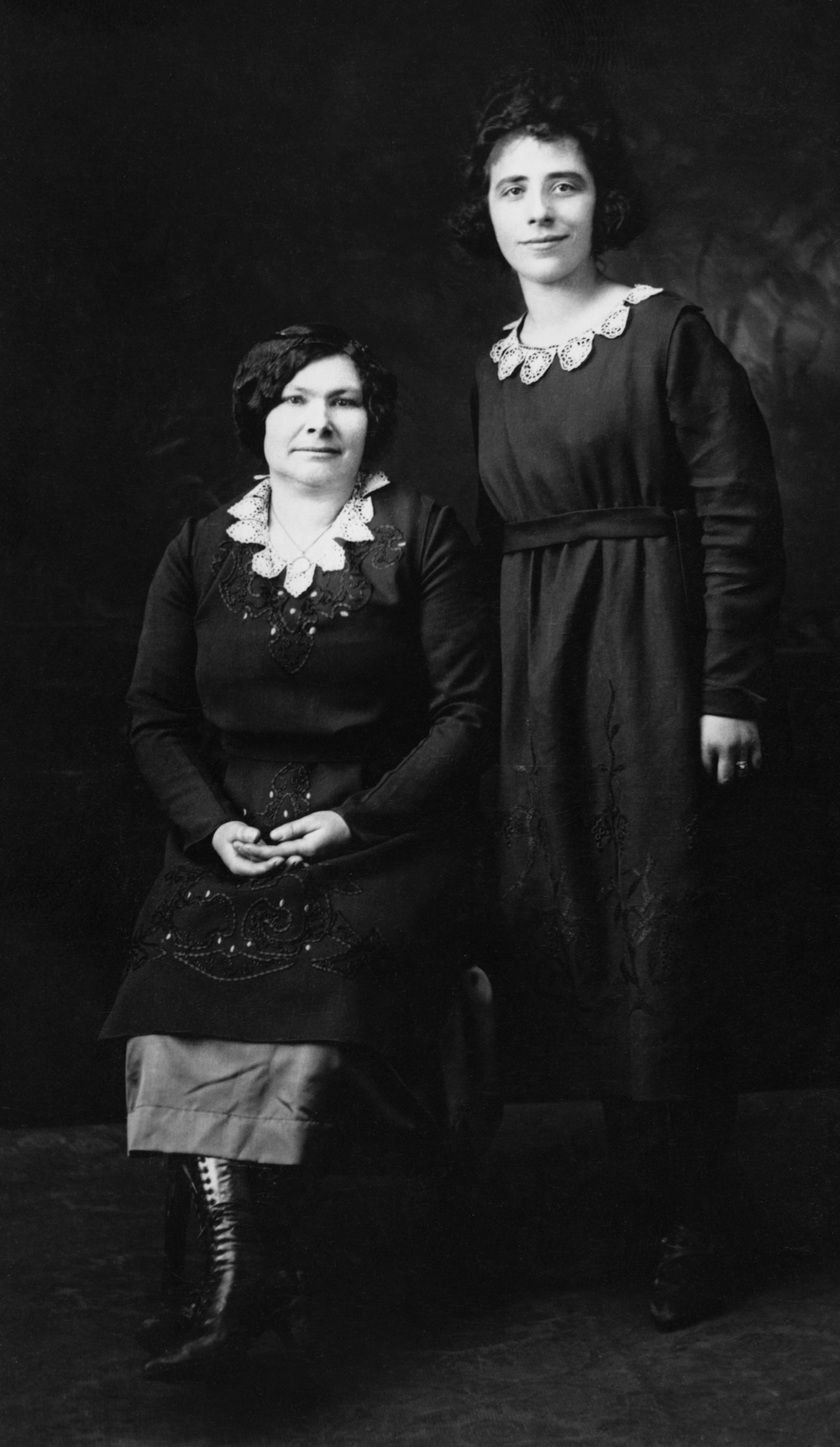 A younger woman standing next to an older woman sitting.