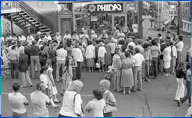 Around twenty women, some young and others older, are sitting in a row along Rue Saint-Eustache, knitting. In front of them, a crowd of about fifty people is watching them.