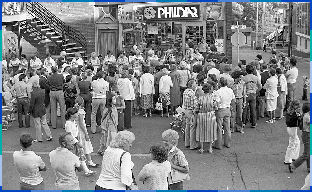 Around twenty women, some young and others older, are sitting in a row along Rue Saint-Eustache, knitting. In front of them, a crowd of about fifty people is watching them.