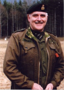 Homme moustachu souriant, cheveux gris en uniforme militaire.