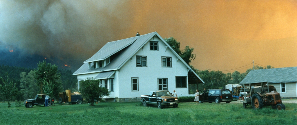 A family evacuates from their home. Fire rages in the background.