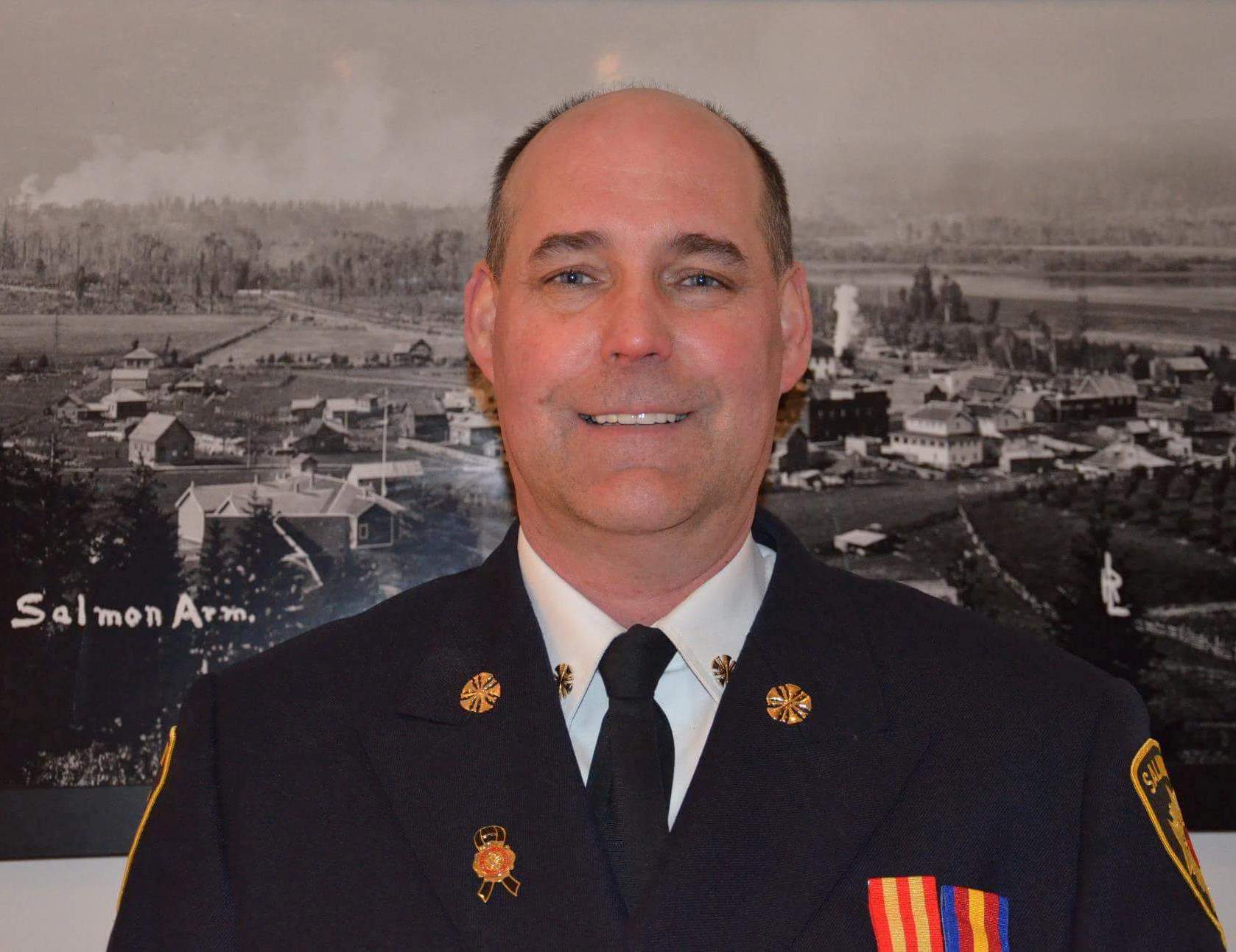 Man in a shirt, tie, and uniform smiles.