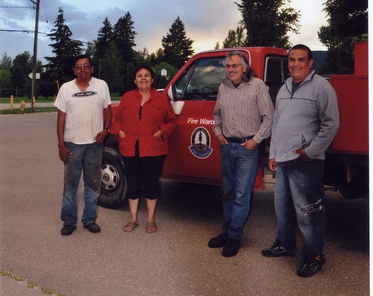 Three men and a woman stand in front of a red truck.
