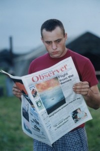 Man stands as he reads the Salmon Arm Observer newspaper. Photo of fire on front cover.