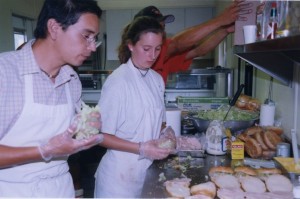 Man and woman in white aprons make sandwiches in a kitchen.