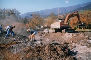 Woman in shorts and three men cleaning up rubble. Backhoe in background.