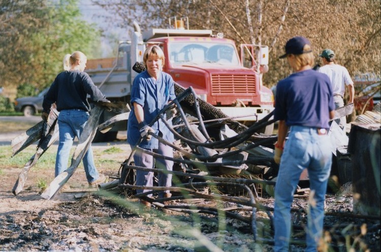 Two women lift twisted metal from a pile. Another teenager carries metal towards a red dump truck.