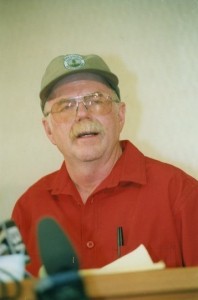 Man wearing a baseball hat speaks to microphones.