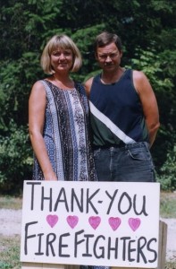 Femme et homme derrière une affiche remerciant les pompiers.