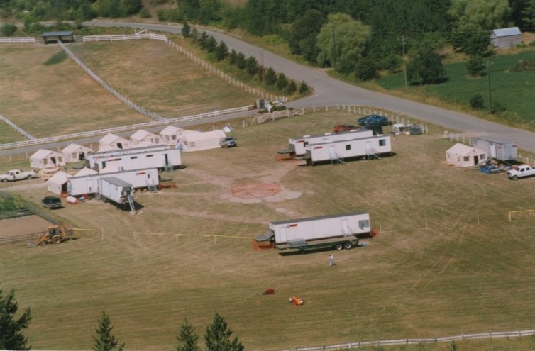 Aerial view of trailers, tents, and a landing pad in a field.
