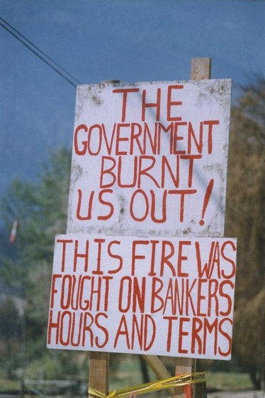 A homemade protest sign painted white with red lettering.