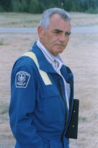 Man in blue coveralls holds a clip board under his arm.