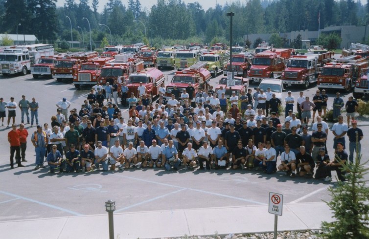 Firefighters assemble in front of fire engines and tenders for a group photo.