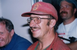 Homme moustachu souriant en combinaison. Coiffé d'une casquette d'officier en gestion de feu.