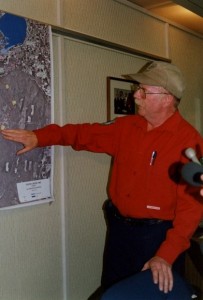 Man points at a place on a map. Two microphones off to the side.