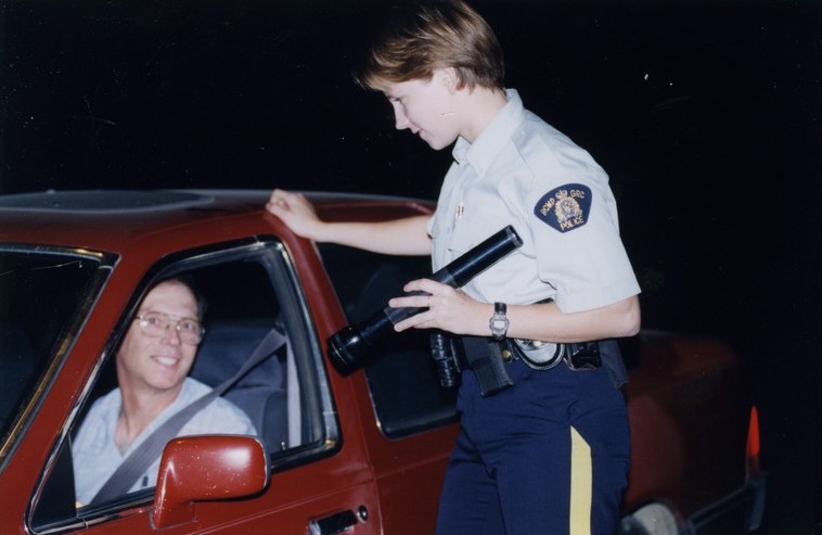 Woman police officer shines flash light at a male driver in a red car.