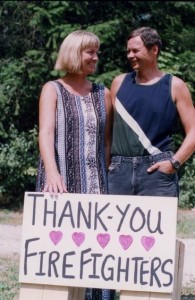 Woman and man smile at each other. She is balancing a sign that says, “Thank you firefighters.”
