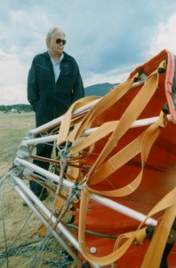 Man in dark blue coveralls and sunglasses stands in front of empty water bucket.