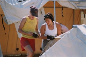 Two women dressed in summer clothing setting up tents.