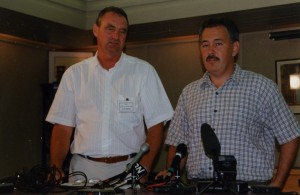 Two men stand in front of microphones.