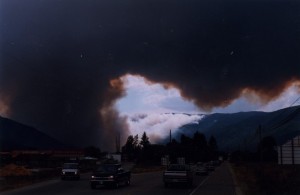 Sky black with smoke as fire burns from one hillside to another.