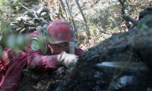 Homme avec combinaison rouge et casque de sécurité asperge avec un boyau d'arrosage.