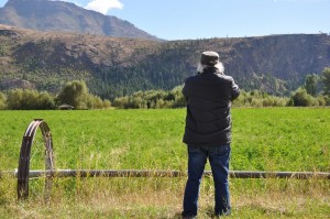 Man stands before a field. Hills in background.