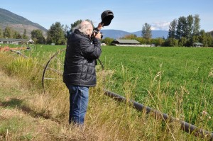 A photographer shooting a scene, shading his lens from the sun.