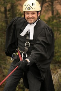 Man in lawyer's robes wearing a helmet with a safety rope around his waist.