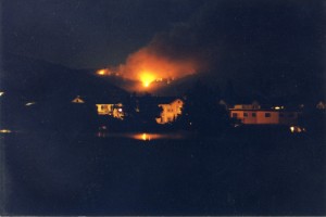 Fire burns bright red at night. Buildings lit in the foreground.