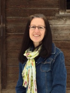 Femme avec lunettes, souriante vêtue d'un veston jean.