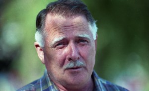 Portrait of a man with short haircut and mustache looks directly at camera.