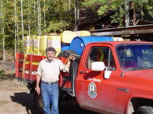 Man stands beside a red truck loaded with supplies.