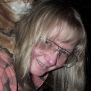 Une femme blonde portant lunettes avec un chat sur ses épaules. 