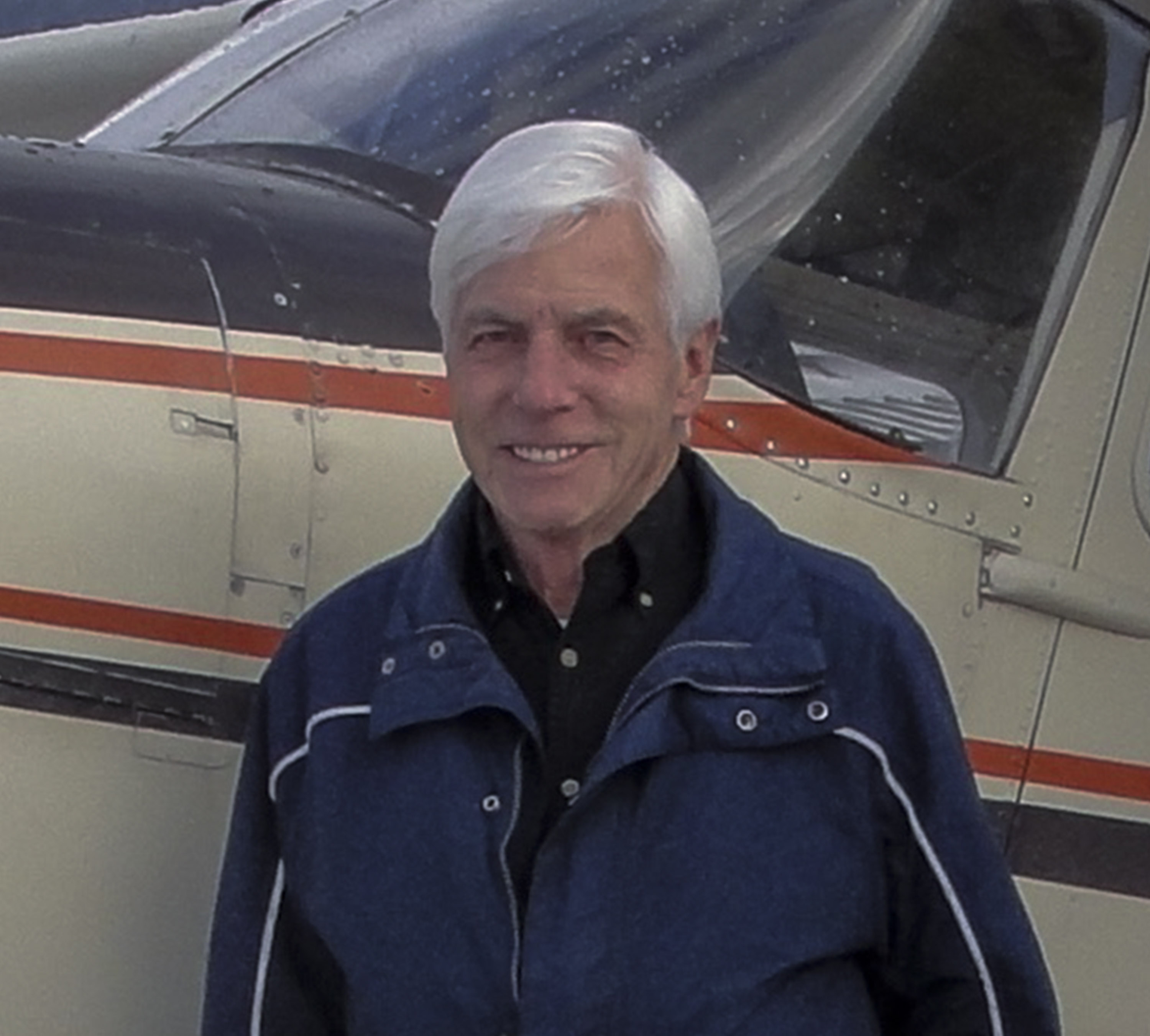 Portrait of a silver haired man standing in front of an aeroplane.