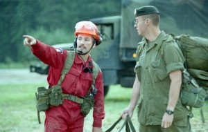 Firefighter directing a soldier in green uniform.