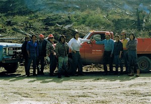 Crew of people stand in front of a red truck.