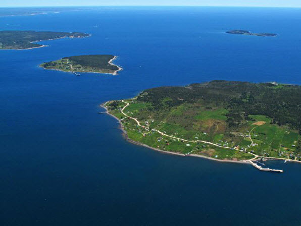 A colour aerial photo of Big and Little Tancook Islands with Big Tancook in the foreground showing the houses and roads; Little Tancook to the left showing roads and houses and to the far left Ironbound Island. The Tancook boat builders were noted designers of schooners and whalers. The fishermen were some of the first to use the make and and break engines to power their boats.