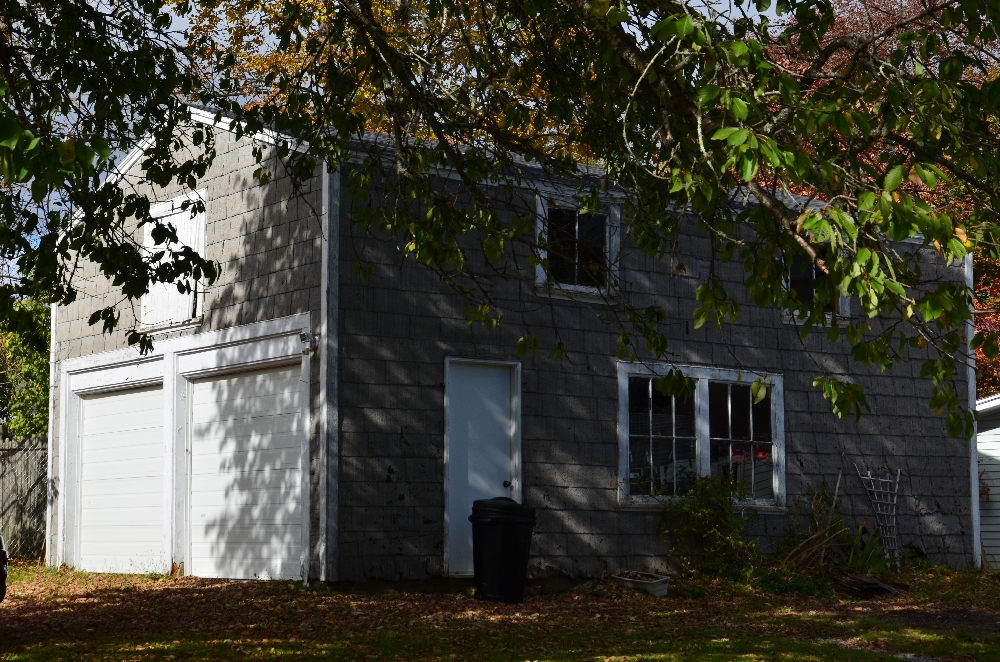 Small grey 2 story building with double garage doors on front and a door and 4 windows on the side which was the first foundry