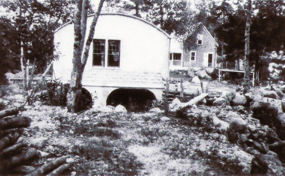 A black and white photo showing the rounded roof of the generating station on the East River, with the river running from under the station. On the right of the generating station, a small house which was where the operator of the generating station lived with his family.